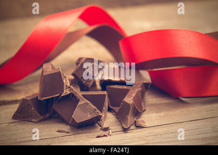 Pezzi di barra di cioccolato con rosso e marrone a nastro su sfondo di legno. Messa a fuoco selettiva Foto Stock