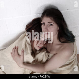Due ragazze tenere su ogni altro per comfort, avvolto in una coperta. Per i superstiti di un disastro, Storm, uragano o terremoto Foto Stock