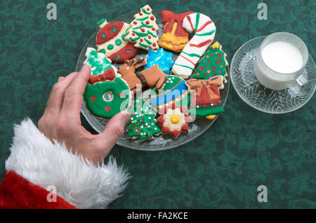 Santa selezionando un ritaglio di Natale Cookie Off della piastra, con un bicchiere di latte Foto Stock