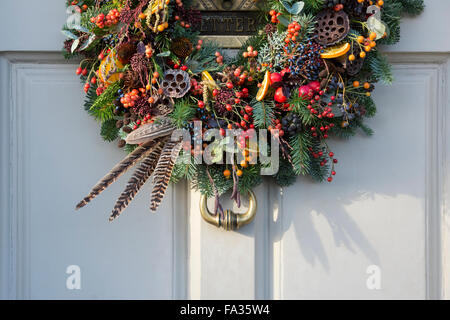 Natale berry, fogliame, giù e frutta corona sulla porta di legno. Cotswolds, Inghilterra Foto Stock