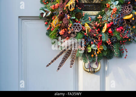 Natale berry, fogliame, giù e frutta corona sulla porta di legno. Cotswolds, Inghilterra Foto Stock