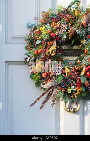 Natale berry, fogliame, giù e frutta corona sulla porta di legno. Cotswolds, Inghilterra Foto Stock