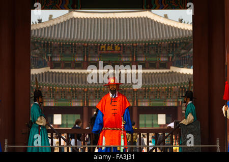 Guardia in rosso abiti tradizionali si erge a incorniciato ingresso nella parte anteriore della gronda del palazzo Gyeongbokgung a Seul, Corea del Sud Foto Stock