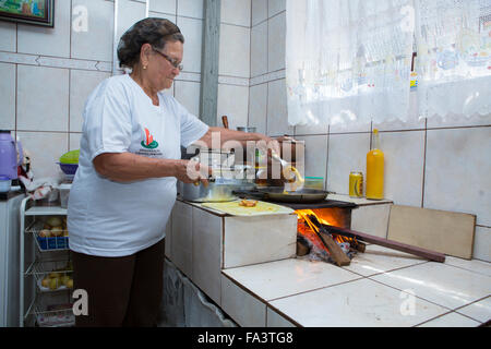 Sud America, Brasile, San Paolo. Una donna locale che cucina il cibo nella sua cucina su un forno a legna tradizionale forno una stufa lenha Foto Stock