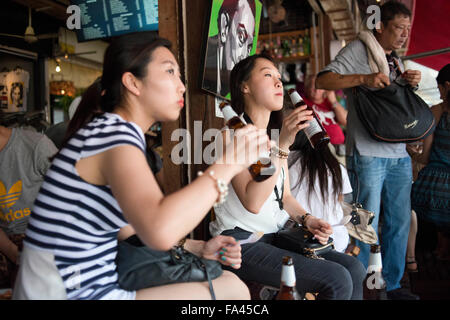 Asian Girls bere birra in viva 8. Chef Fernando Andrés Yusta in posa vicino al sea food padella per paella, Mercato del fine settimana di Chatuchak. Chatucha Foto Stock