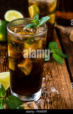 Longdrink freddo (Cuba Libre) marrone con il rum e lime fresco rustico sfondo di legno Foto Stock