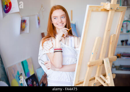 Felice ispirato sorridente artista femminile con lunghi capelli rossi disegno con matita in classe d'arte Foto Stock