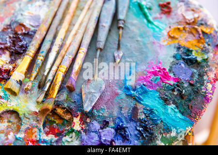 Immagine di sfondo di luminosi colori misti vernici su arte tavolozza con pennelli e spatole Foto Stock