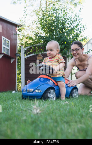 Baby boy equitazione sulla macchina giocattolo con sua madre spingendolo da dietro, Monaco di Baviera, Germania Foto Stock