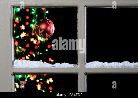 Pallina e albero attraverso la finestra con neve sul telaio. Foto Stock