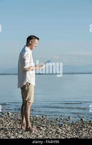 Uomo maturo la lettura del libro e sorridente a Lakeside, Baviera, Germania Foto Stock