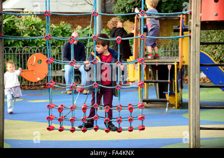 Un ragazzo si arrampica su una rete da arrampicata che è parte di un telaio di arrampicata in un parco giochi per bambini. Foto Stock