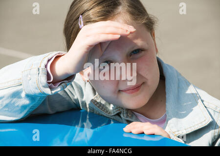 Ritratto di ragazza in piedi nel parco giochi scuola gli occhi di ombreggiatura da Sun, Foto Stock