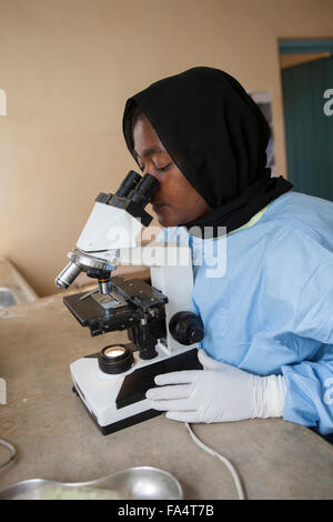 Un assistente di laboratorio opera un microscopio a energia solare di centro di salute della regione di Kigoma, Tanzania occidentale. Foto Stock