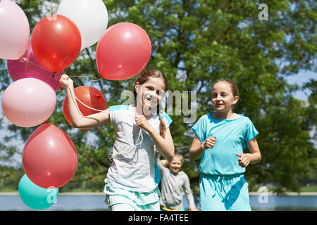 Le ragazze in esecuzione nel parco con palloncini, Lago Karlsfeld di Monaco di Baviera, Germania Foto Stock