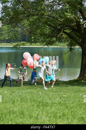 I bambini in esecuzione nel parco con palloncini, Monaco di Baviera, Germania Foto Stock