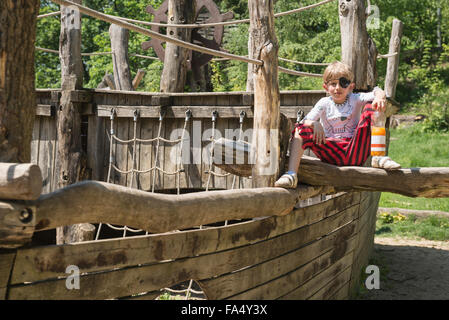 Ragazzo seduto sulla riproduzione pirata nave nel parco giochi avventura, Baviera, Germania Foto Stock