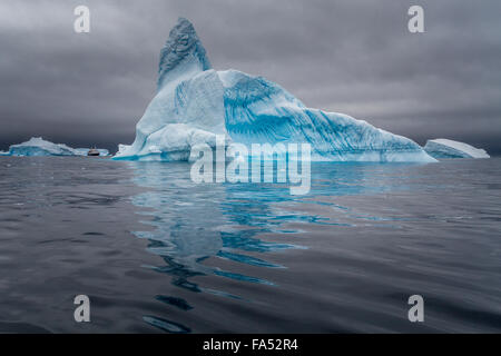 Enormi iceberg con una nave da crociera per il confronto delle dimensioni, impostare off vibrante contro la moody sky, Antartide Foto Stock