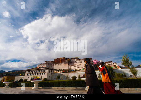 Due femmina pellegrini tibetani vestiti in abito tradizionale camminando sul marciapiede e guardando la facciata anteriore del palazzo del Potala Foto Stock