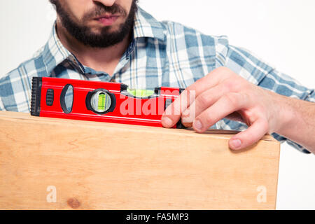 Close up concenrated barbuto giovane uomo in plaid shirt utilizzando la livella su sfondo bianco Foto Stock