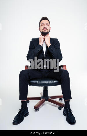 Ritratto di grave concentrata young business man in black tuta e scarpe in nero la sedia da ufficio su sfondo bianco Foto Stock
