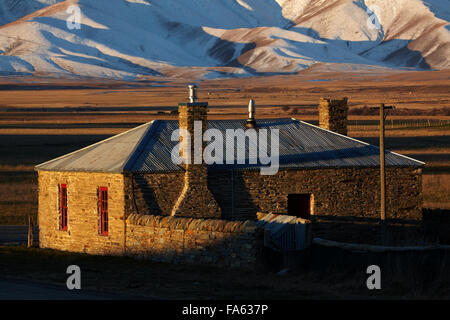 Storico cottage in pietra e gamma di Ida in inverno, Colline Creek, Maniototo di Central Otago, Isola del Sud, Nuova Zelanda Foto Stock