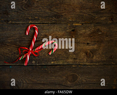 Primo piano di due in vecchio stile candy canes su un rustico sfondo di legno. Le chicche sono incrociate e legate con un nastro rosso Foto Stock