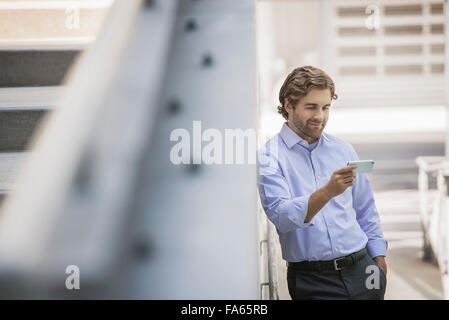 Un Uomo in camicia e cravatta utilizzando uno smart phone in una scena urbana. Foto Stock