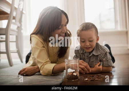 Una donna e un bambino sdraiato sul pavimento, giocando con ottone e monete d'argento, inserirli in un vasetto di vetro. Foto Stock