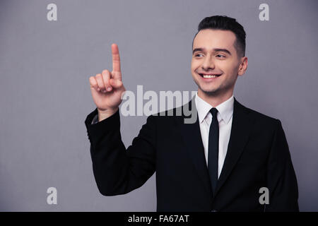 Ritratto di un imprenditore sorridente puntare il dito su sfondo grigio Foto Stock