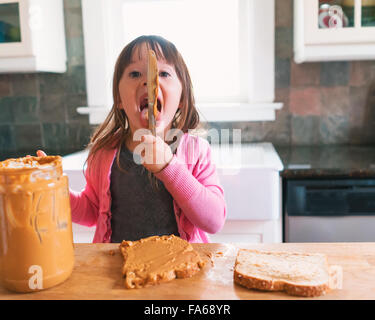 Ragazza facendo un sandwich al burro di arachidi, leccare il coltello Foto Stock