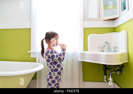 Vista laterale della ragazza la spazzolatura dei denti nella stanza da bagno Foto Stock