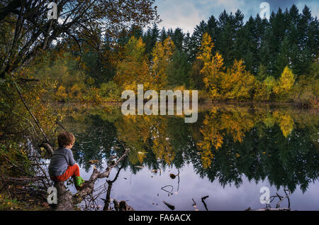 Ragazzo seduto sul tronco di albero dal lago Foto Stock