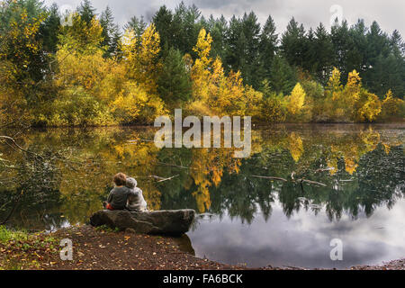 Un ragazzo e una ragazza seduta su una roccia da un lago Foto Stock