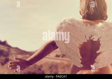 Vista posteriore di una donna che indossa un paio di ali d'angelo con le braccia tese Foto Stock