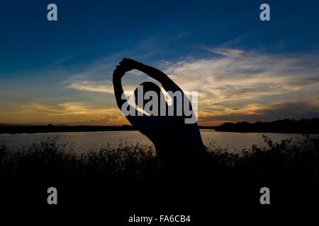 Uomo seduto dal lago facendo esercizi yoga al tramonto Foto Stock