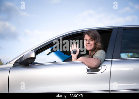 Ragazza adolescente seduto in un auto tenendo premuto i tasti fino alla nuova vettura Foto Stock