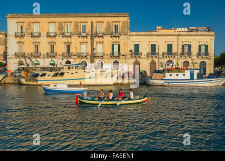 Uomini canottaggio Mediterraneo, vista di una squadra di canottaggio che si dirige su uno stretto canale che separa Ortigia dalla città di Siracusa, Sicilia. Foto Stock