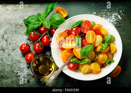 Pomodori freschi con le foglie di basilico in una ciotola su sfondo vintage. Foto Stock