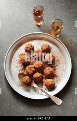 Tartufi di cioccolato su una piastra di alluminio con 2 bicchieri di liquore sullo sfondo Foto Stock