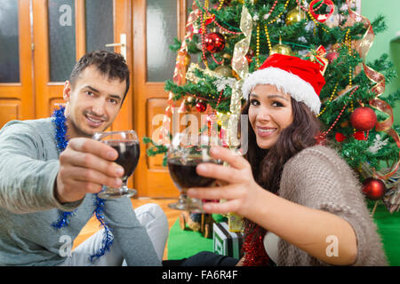 Coppia attraente godendo il tempo di Natale bevendo vino celebrando , due persone spendere nuovo anno a casa da albero di Natale wi Foto Stock