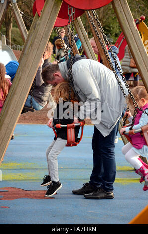 Un padre aiuta a sua figlia su un altalena nel parco. Foto Stock