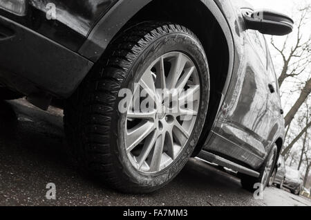 Primo piano ad angolo ampio frammento foto di auto nera, ruota in lega leggera con pneumatici invernali sulla città sporca road. Messa a fuoco selettiva e dovrà Foto Stock