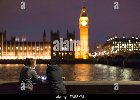 Vista posteriore di giovani donne utilizza lo smartphone di fronte Palazzo di Westminster, Londra, Regno Unito Foto Stock