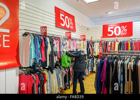 Una donna che guarda i vestiti in una vendita appeso su rotaie in un negozio con il 50% di sconto prezzi Foto Stock