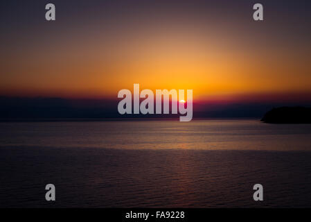 Il sorgere del sole sul mare con splendido vibrante bagliore rosso. Le montagne sullo sfondo. Foto Stock