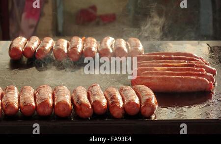 Un venditore ambulante arrosti freschi salsicce di maiale alla griglia Foto Stock