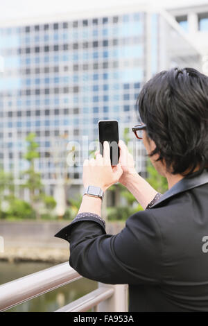 Imprenditore giapponese con smart indossabile guarda e lo smartphone Foto Stock