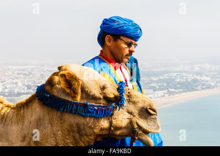 Driver di cammello sulla montagna di fronte alla baia di Agadir, Marocco Foto Stock