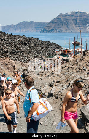 Santorini, Erinia Bay, Nea Kameni. I turisti a piedi al bordo del vulcano dal porto lungo ruvida percorso roccioso attraverso il paesaggio desolato sotto il sole caldo. Foto Stock